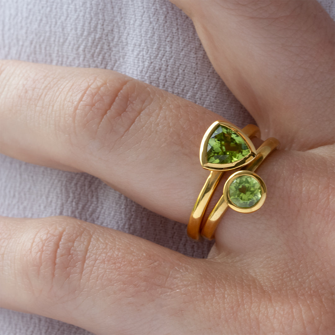 Mano con Combinación de 2 anillos de Oro Vermeil amarillo, con piedras peridoto natural tallada en forma triangular y brillante.