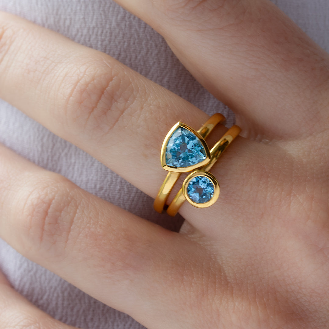 Mano con Combinación de 2 anillos de Oro Vermeil amarillo, con piedras topacio azul natural tallada en forma triangular y brillante.