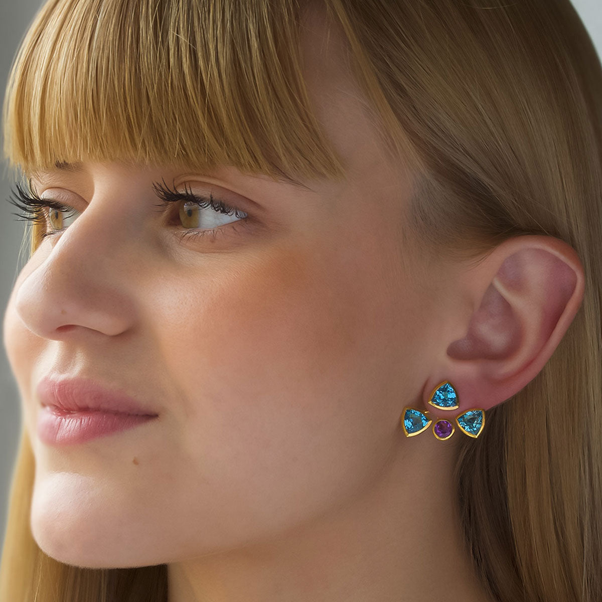 Modelo con Pendiente desmontable tipo “ear jacket” de Oro Vermeil amarillo, 3 topacios azules naturales talla trillion de 7 x 7mm y 1 amatista talla brillante de 5mm de diámetro. 