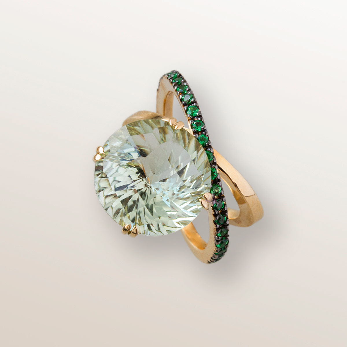 Anillo de oro amarillo de 750 milésimas con dos órbitas cuajadas de 21 tsavoritas verdes de 2 milímetros y en el centro una gran piedra de Cuarzo verde Prasiolita en talla redonda fantasía.