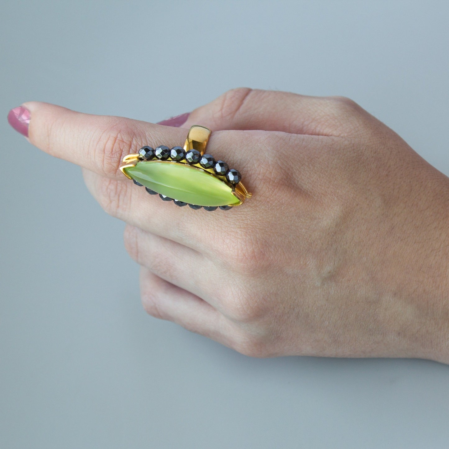 Mano luciendo el anillo de Oro Vermeil amarillo, con un Ágata color verde manzana talla marquise cabujón. Rodeada de 18 hematites facetados.