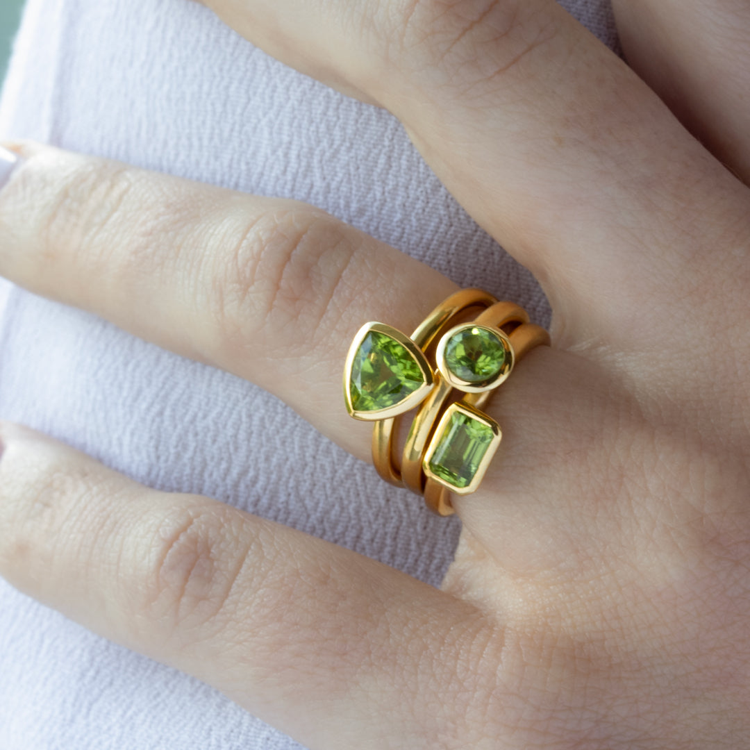 Mano con Combinación de 3 anillos de Oro Vermeil amarillo, con piedras peridoto natural tallada en forma triangular, brillante y octogonal.