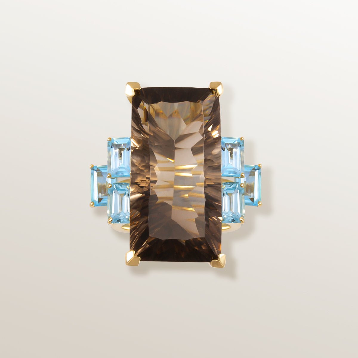 Anillo de oro amarillo de 750 milésimas con gran Cuarzo ahumado color chocolate en talla rectangular en el centro, y piedras laterales Topacio Swiss Blue de color azul cielo.