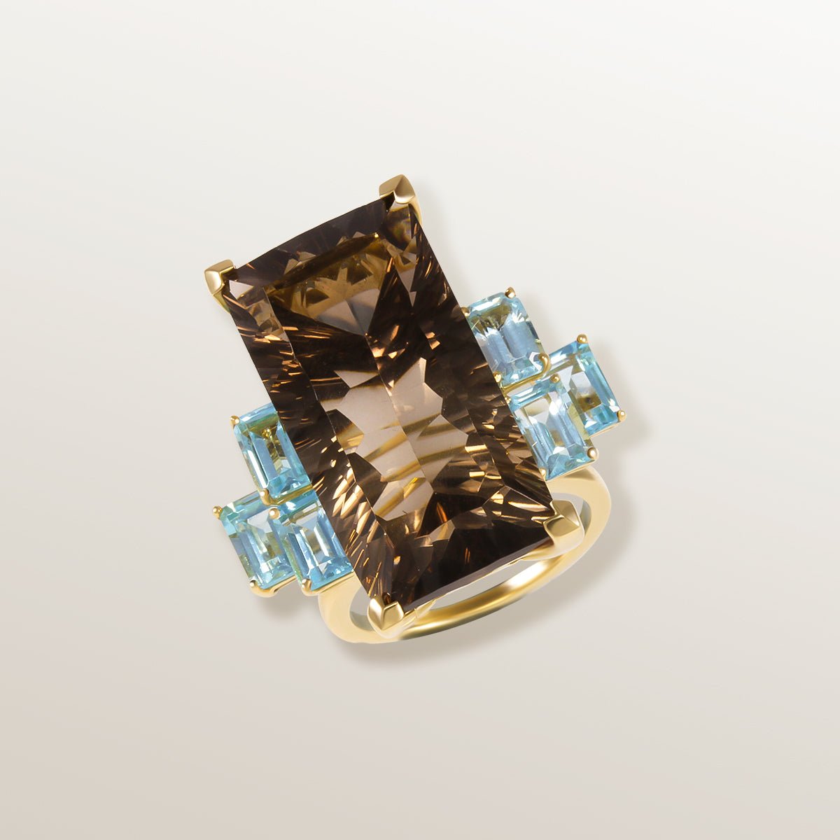 Anillo de oro amarillo de 750 milésimas con gran Cuarzo ahumado color chocolate en talla rectangular en el centro, y piedras laterales Topacio Swiss Blue de color azul cielo.