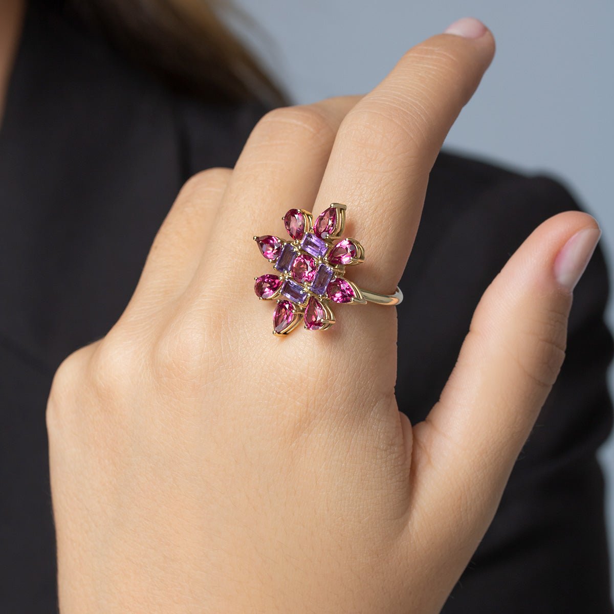 Mano con Anillo de oro amarillo con forma de estrella cuajada de topacios rosa y amatistas.