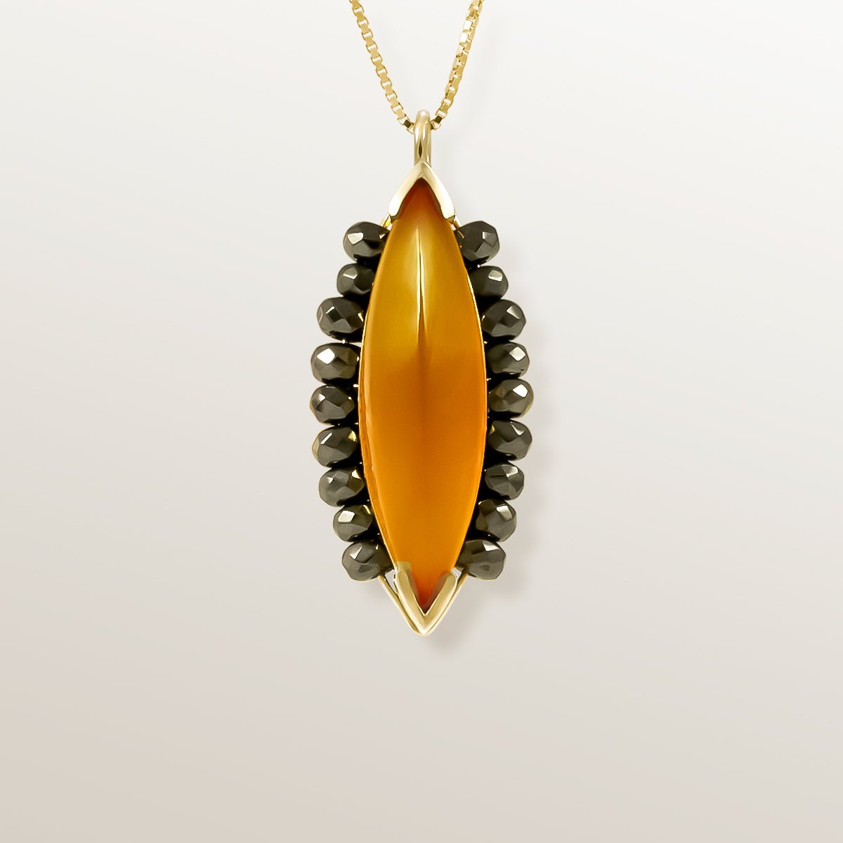 Colgante de Oro Vermeil amarillo, con un Ágata color miel, talla marquise cabujón. Rodeada de 18 Hematites facetados.