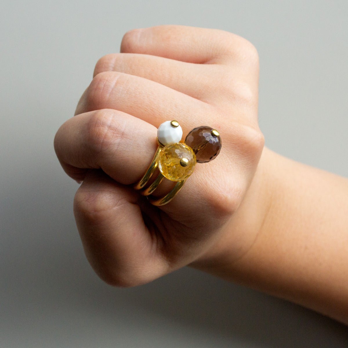 Mano con Combinación de 3 anillos de Oro Vermeil amarillo, con piedra natural Ágata Blanca de 8 mm, Cuarzo Ahumado de 12 mm y Citrino Marmolado de 12 mm.